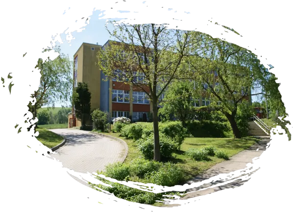 The red-painted building of the Förderschule Polenz, in the back of a green meadow with trees and bushes